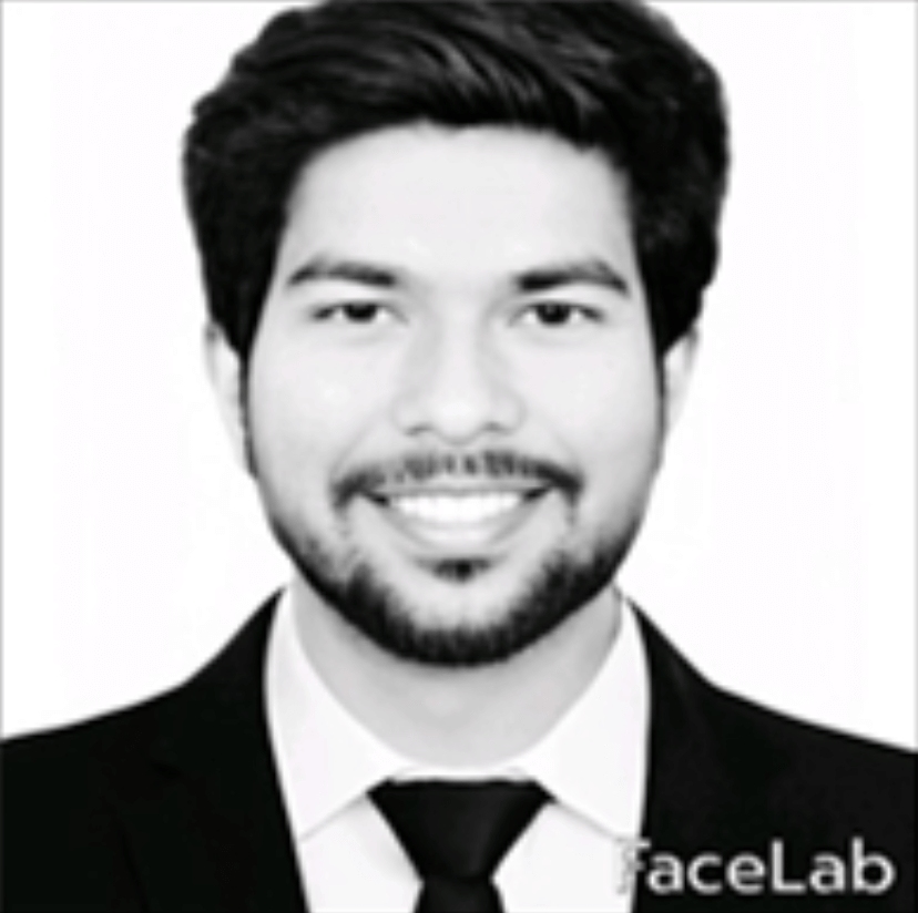 A man with short dark hair and a beard is smiling. He is wearing a dark suit, white shirt, and a tie. The background is plain white, and the image is in black and white. The word "FaceLab" appears in the corner.
